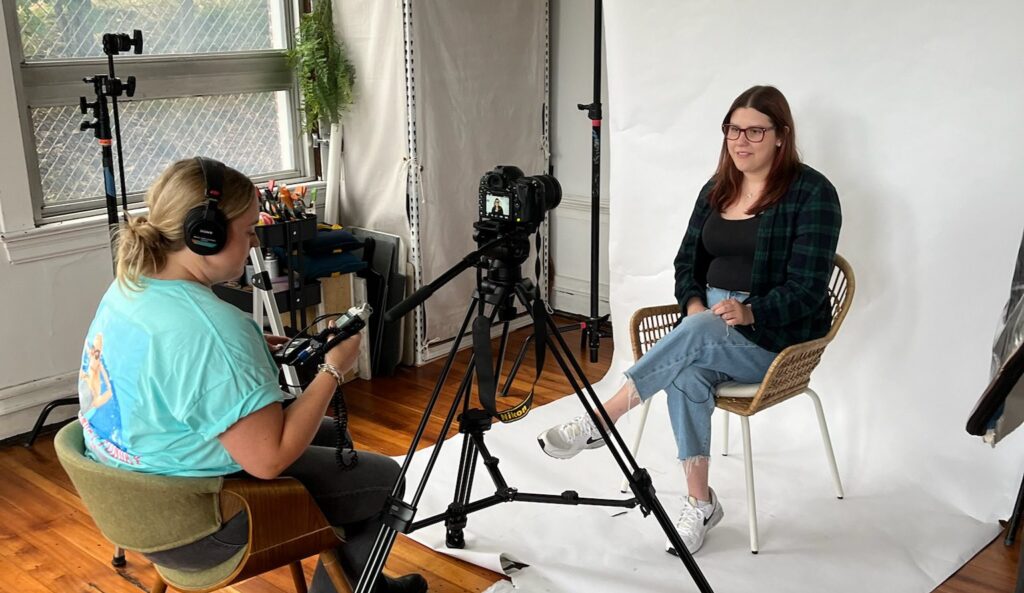 Photographer taking photos and videos of client in front of white backdrop at photo studio in Massachsuetts.