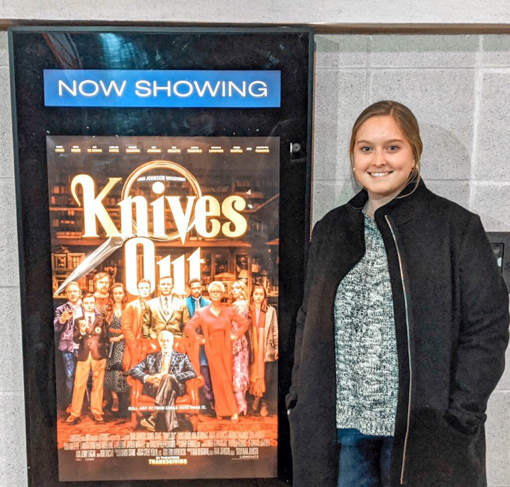 Emma of Emma Lula Creative posing with poster for Knives Out at movie theater in Foxboro, MA
