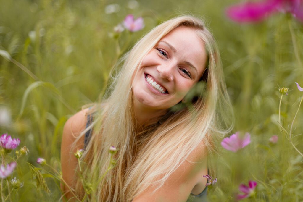 Woman smiling at camera in field of flowers for portrait session in Medfield, Massachusetts with Emma Lula Creative.