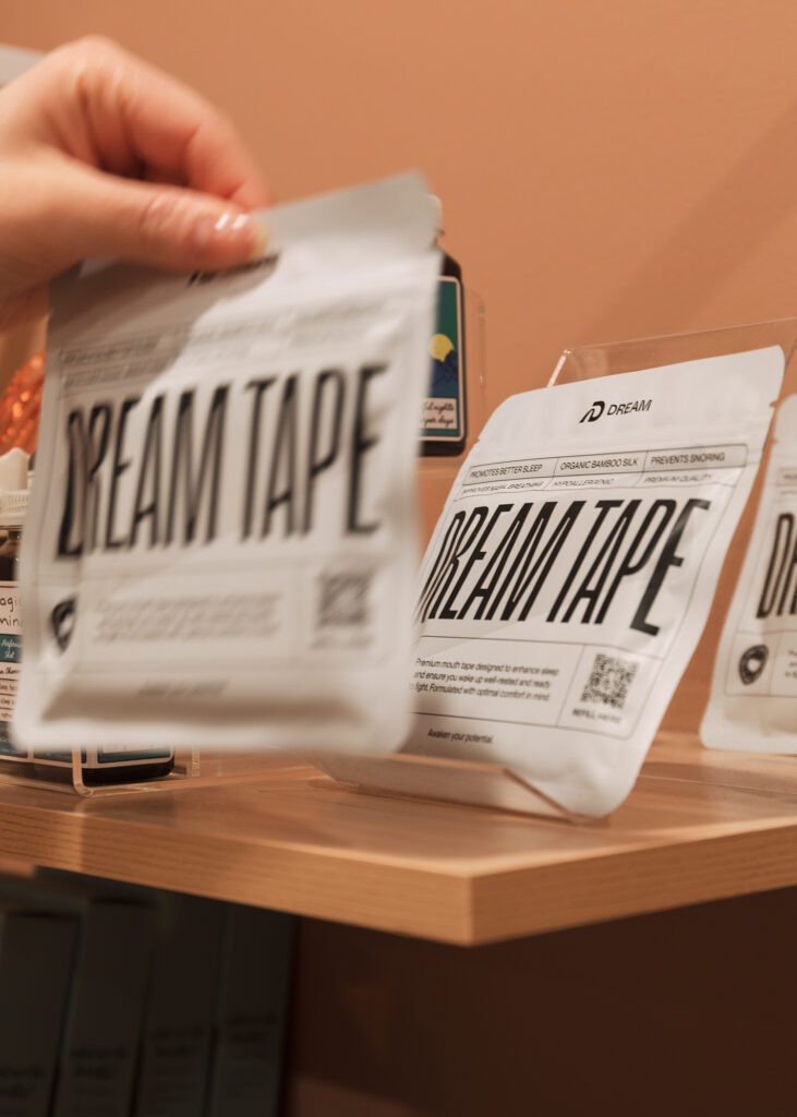 Woman picking Dream Tape product off of shelf of products for branding photography session in Revival Wellness Studio in Medfield, Massachusetts.