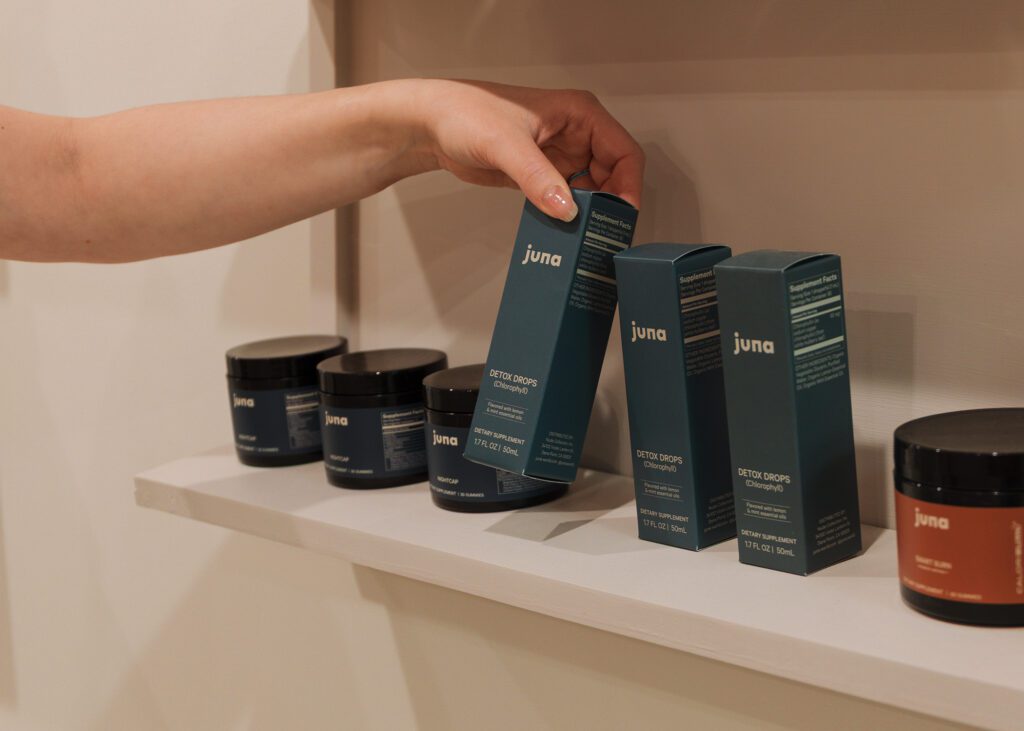 Woman picking up Juna box from shelves of products for branding photography session in Revival Wellness Studio in Medfield, Massachusetts.