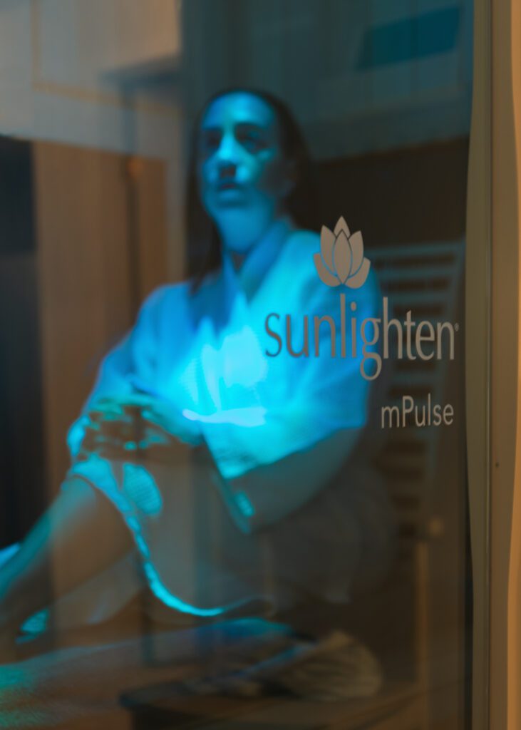 Looking through sunlighten mPulse sauna to woman in robe for branding photography session in Revival Wellness Studio in Medfield, Massachusetts.